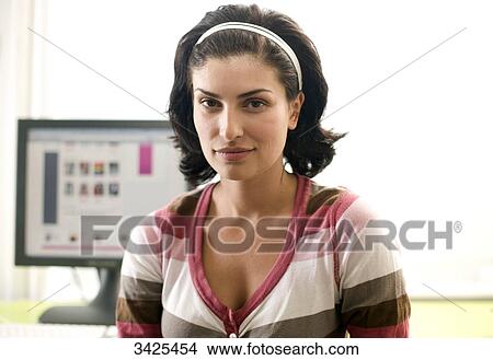 Picture - Young woman sitting in front of a computer monitor, portrait . Fotosearch
