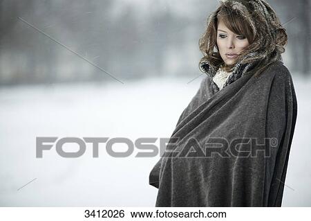 Stock Photograph - Young woman standing with poncho in snow . Fotosearch