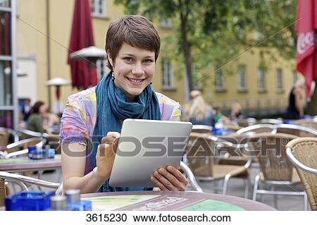 Stock Image - Young woman using iPad at an outdoor cafe . Fotosearch