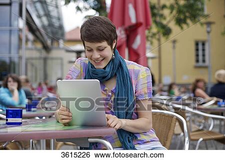 Stock Photograph - Young woman using iPad at an outdoor cafe . Fotosearch