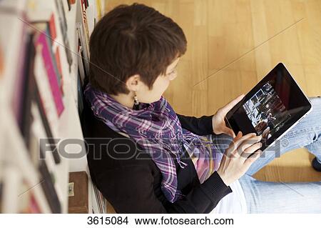 Picture - Young woman using iPad in front of bookshelf . Fotosearch