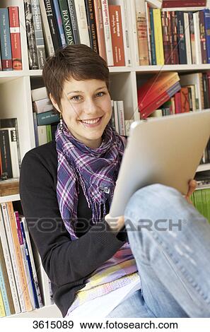 Young woman using iPad in front of bookshelf View Large Photo Image Stock Photo - Young woman using iPad in front of bookshelf . Fotosearch