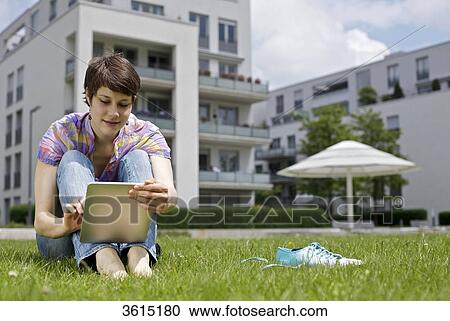 Stock Image - Young woman using iPad in grass . Fotosearch
