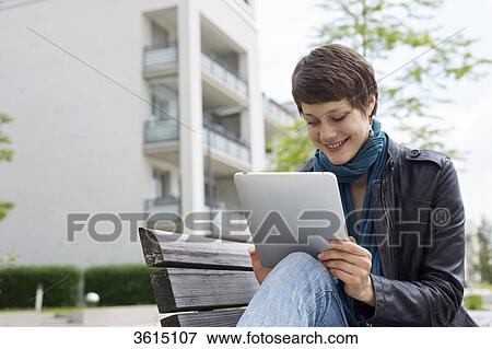 Young woman using iPad on a bench View Large Photo Image Stock Photo - Young woman using iPad on a bench . Fotosearch
