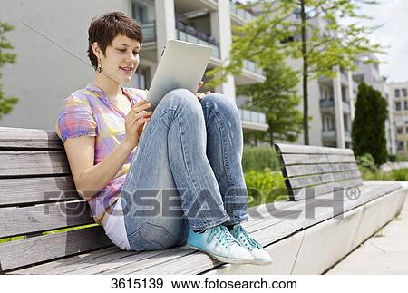Young woman using iPad on a bench View Large Photo Image Stock Photo - Young woman using iPad on a bench . Fotosearch