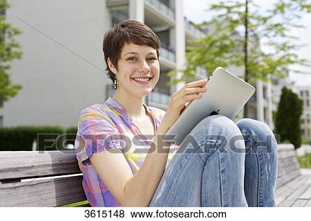Stock Photo - Young woman using iPad on a bench . Fotosearch