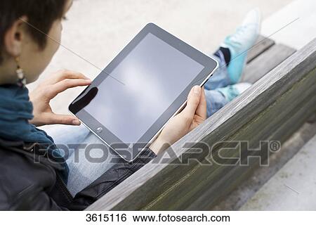 Stock Photograph - Young woman using iPad on a bench . Fotosearch
