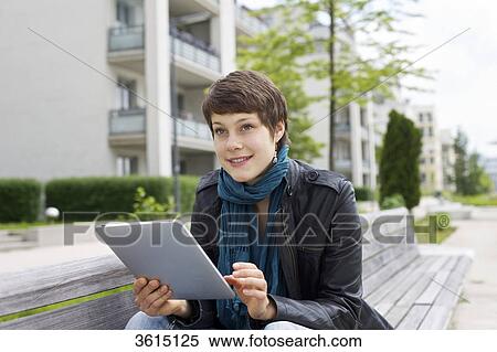 Stock Photography - Young woman using iPad on a bench . Fotosearch