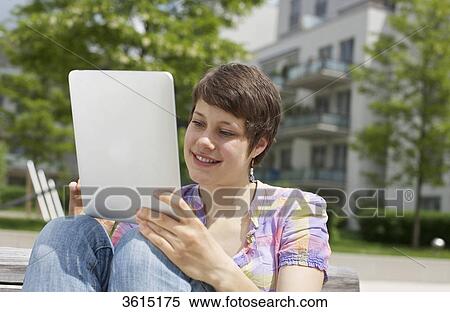 Stock Photography - Young woman using iPad on a bench . Fotosearch