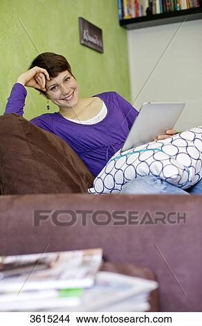 Young woman using iPad on couch View Large Photo Image Picture - Young woman using iPad on couch . Fotosearch