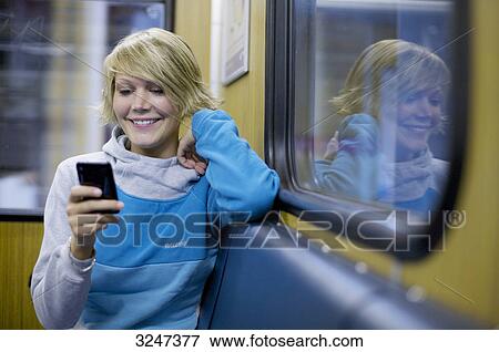 Stock Photo - Young woman using mobile phone in city train, front view . Fotosearch