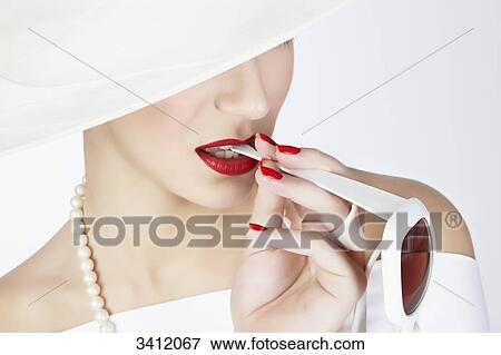 Stock Photo - Young woman with white hat biting on sunglasses . Fotosearch
