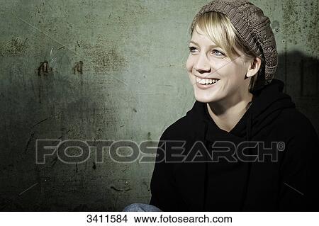 Young woman with woollen cap sitting in front of a gate, portrait View Large Photo Image Picture - Young woman with woollen cap sitting in front of a gate, portrait . Fotosearch