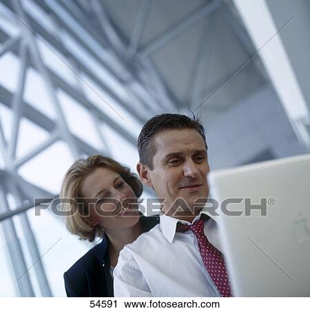 Stock Image - Businessman and businesswoman looking at laptop . Fotosearch