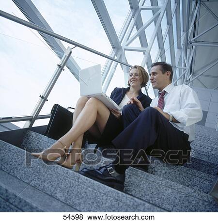Stock Photo - Businessman and businesswoman looking at laptop on stairs . Fotosearch