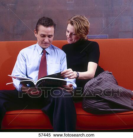 Stock Photography - Businessman and businesswoman reading magazine on a couch . Fotosearch