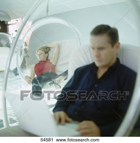 Stock Image - Businessman using laptop with young woman in background . Fotosearch