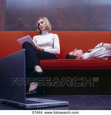 Picture - Businesswoman reading documents with businessman sleeping on a couch . Fotosearch