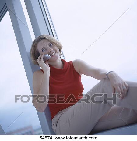 Businesswoman using mobile phone and sitting on windowsill View Large Photo Image Picture - Businesswoman using mobile phone and sitting on windowsill . Fotosearch