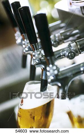 Stock Image - Close-up of a glass under the taps of draught beer . Fotosearch