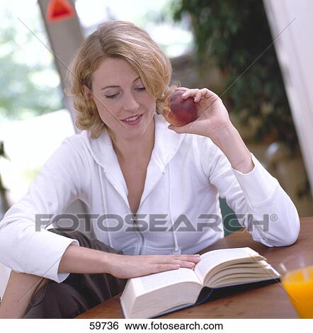 Stock Photograph - Close-up of a young woman reading book and holding peach . Fotosearch