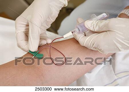 Stock Image - Close-up of person's hands taking blood sample from patient's arm . Fotosearch
