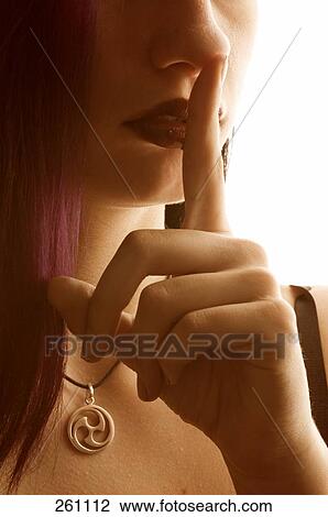 Stock Image - Close-up of young woman with her finger on her lips . Fotosearch