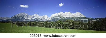 Stock Image - Grassy landscape with mountain range in background, Austria . Fotosearch