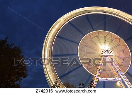 Lit up fairground ride in motion at amusement park during dusk, Germany View Large Photo Image Stock Photograph - Lit up fairground ride in motion at amusement park during dusk, Germany . Fotosearch