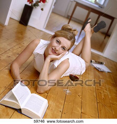 Stock Photograph - Portrait of a young woman lying on floor with book . Fotosearch