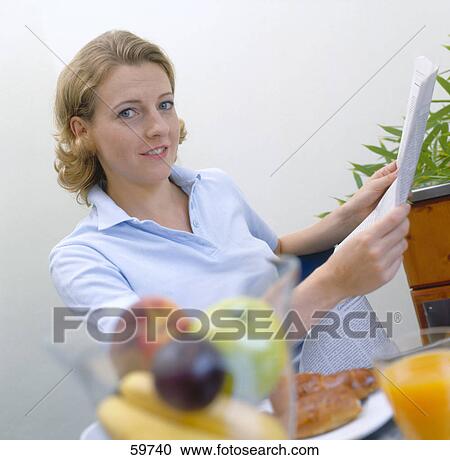 Stock Image - Portrait of a young woman reading the newspaper at breakfast table . Fotosearch