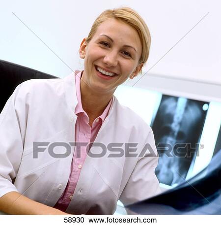 Stock Image - Portrait of female doctor holding x-ray image and smiling . Fotosearch