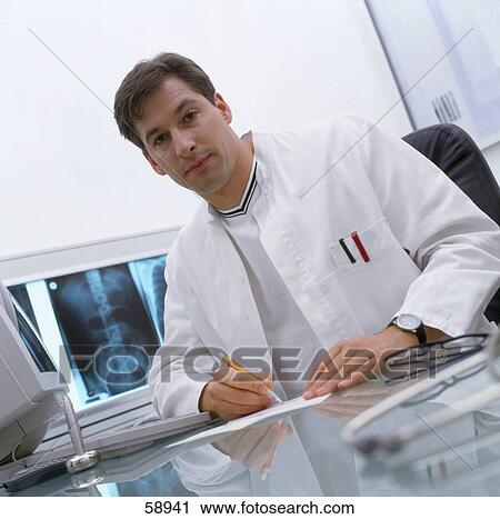 Stock Image - Portrait of male doctor writing on paper in hospital . Fotosearch