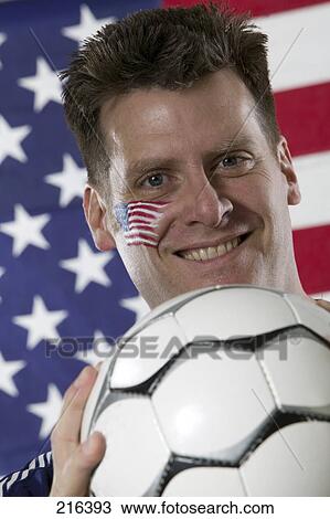 Stock Image - Portrait of male soccer fan holding soccer ball and smiling . Fotosearch