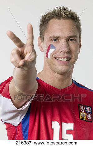 Stock Photo - Portrait of male soccer fan showing victory sign and smiling . Fotosearch
