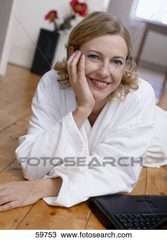Stock Image - Portrait of young woman lying on floor with laptop . Fotosearch