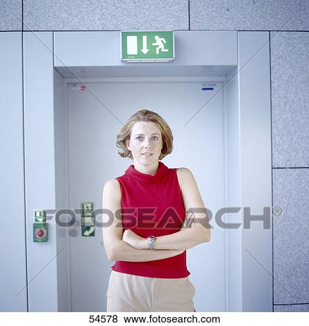 Stock Photo - Portrait of young woman standing in front of door . Fotosearch