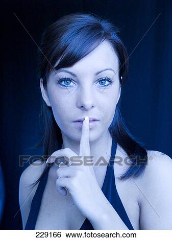 Stock Photograph - Portrait of young woman with her finger on her lips . Fotosearch