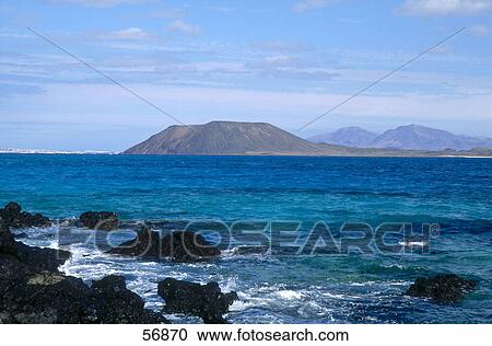 Stock Image - Rock formation on the coast with mountains in the background . Fotosearch
