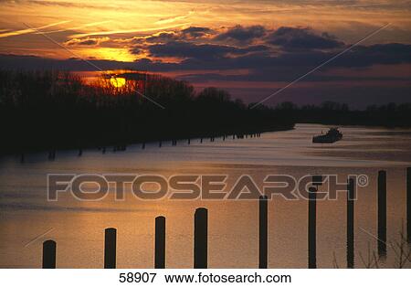 Stock Photo - Silhouette of barge in river at sunset, Elbe River, Germany . Fotosearch