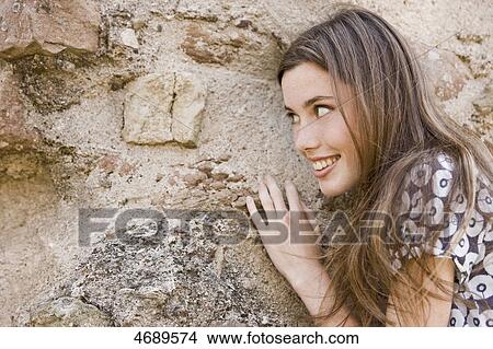 Picture - Smiling young woman with long brown hair at stone wall . Fotosearch
