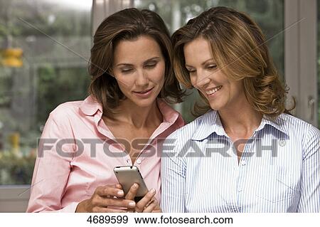 Two smiling women holding cell phone View Large Photo Image Stock Photo - Two smiling women holding cell phone . Fotosearch