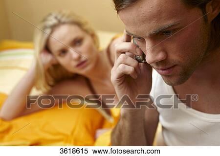 Stock Photography - Woman in bed looking at man on cell phone . Fotosearch