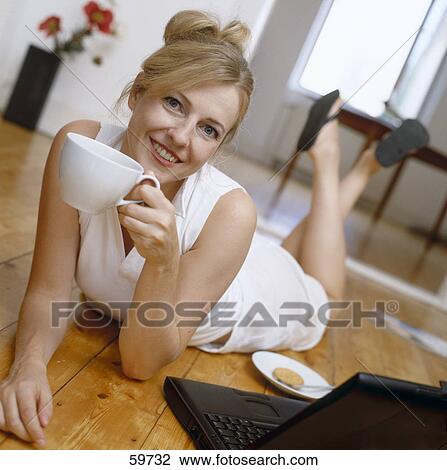 Stock Image - Woman lying on floor and drinking coffee . Fotosearch