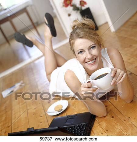 Stock Photo - Woman lying on floor and drinking coffee, low angle view . Fotosearch
