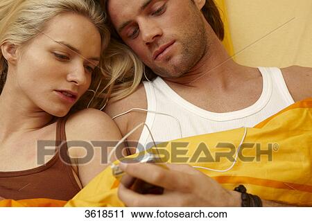 Stock Image - Young couple in bed with mp3 player . Fotosearch
