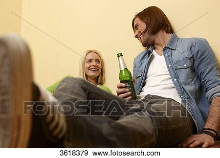 Stock Photo - Young couple sitting on floor drinking beer . Fotosearch