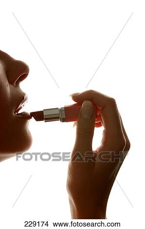 Picture - Young woman applying lipstick on lips, side view . Fotosearch