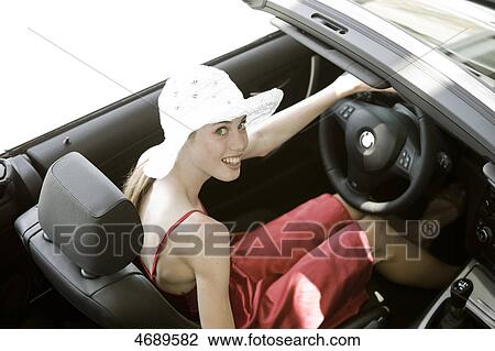 Stock Image - Young woman wearing red dress in a convertible . Fotosearch