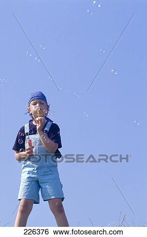 Boy blowing bubbles against clear blue sky View Large Photo Image Stock Photograph - Boy blowing bubbles against clear blue sky . Fotosearch